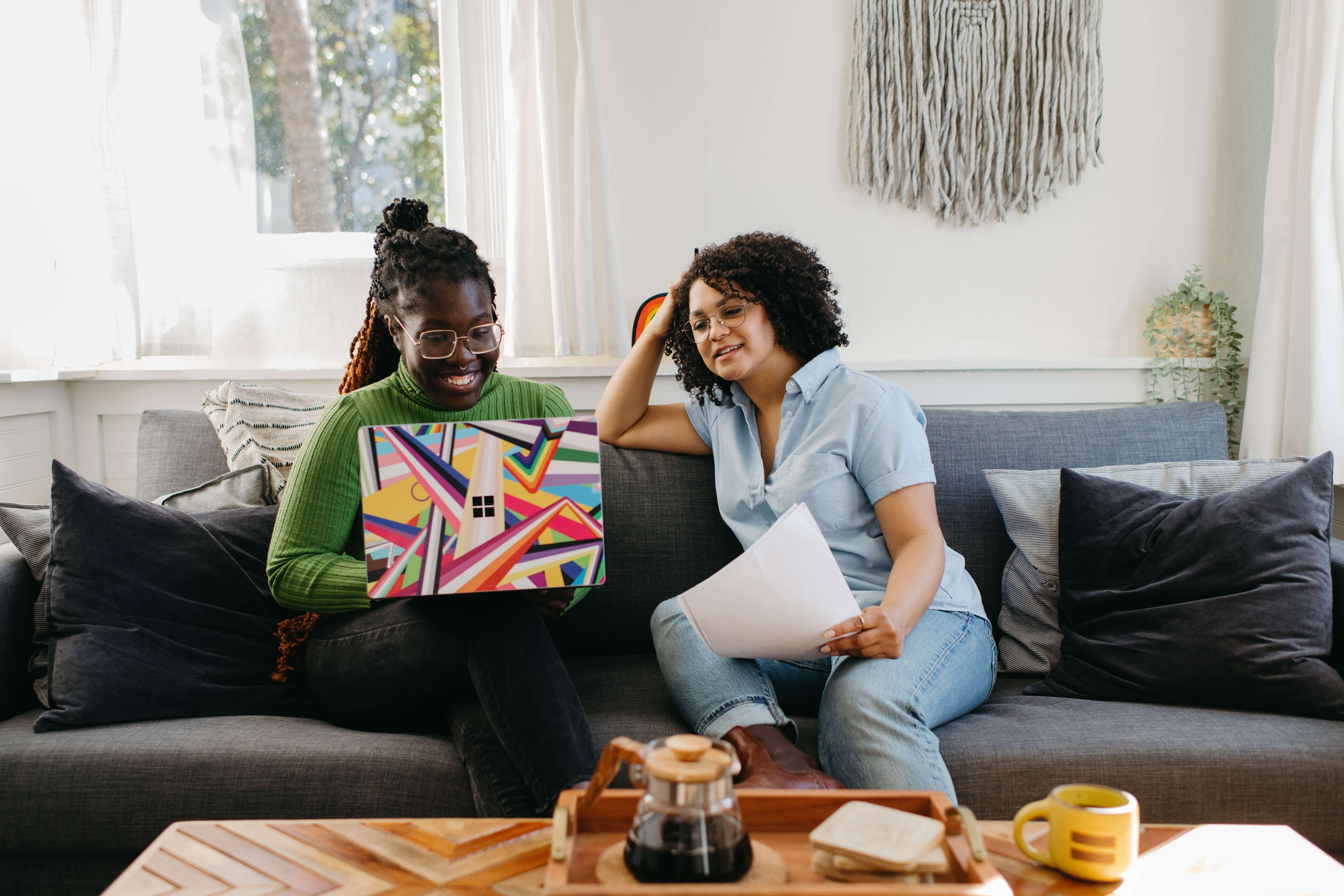 two women working on a computer on the couch